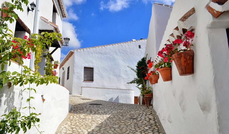 Whitewashed street in El Acebuchal village near Frigiliana, Málaga, with painted pots and the Sierra Almijara mountains behind